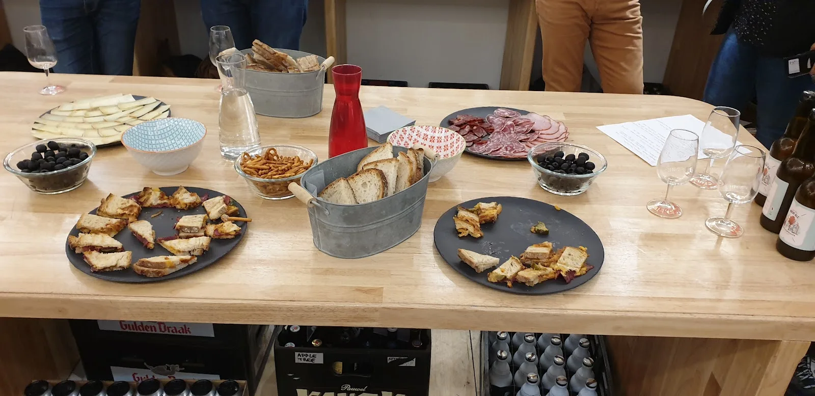 Une grande table en bois à L'Instant T couverte de planches à partager : charcuterie, olives, bretzels, pain et verres